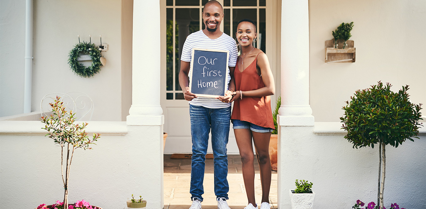 young couple standing in front of first home
